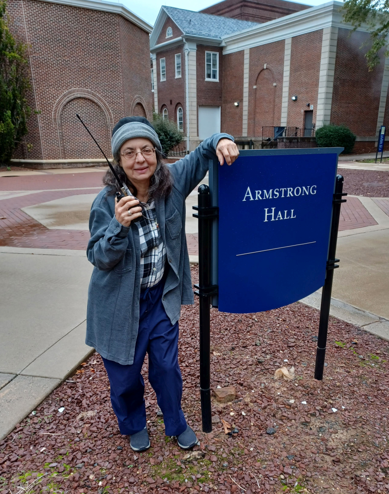 Rebecca, K3RPM stands next to a sign reading "Alexander Hall" in front of that building at TCNJ.
